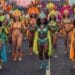 A vibrant image shows a performer at the Notting Hill Carnival wearing an elaborate costume with a large feather headdress